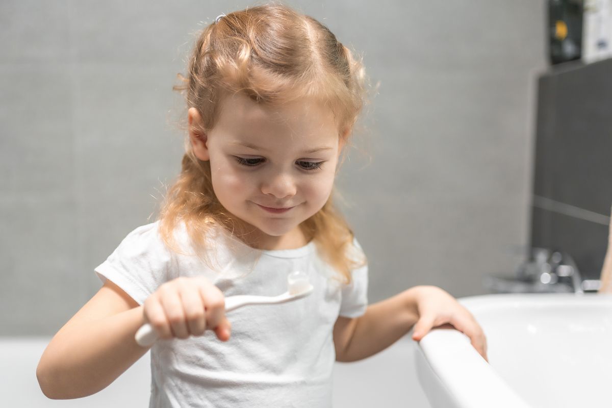 Young child holding a toothbrush in a bathroom, learning healthy brushing habits as part of a daily oral hygiene routine.