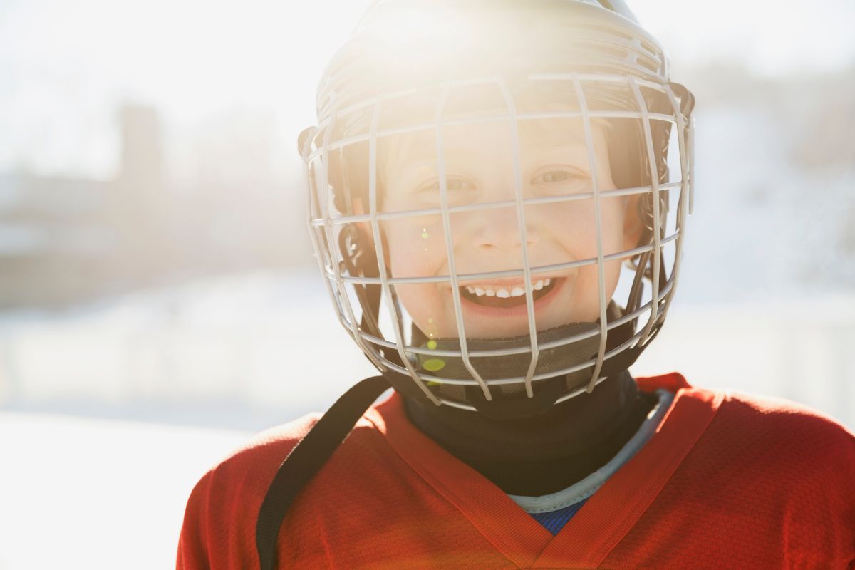 A young athlete smiles while wearing a protective sports helmet, highlighting the importance of safeguarding teeth during youth sports activities.