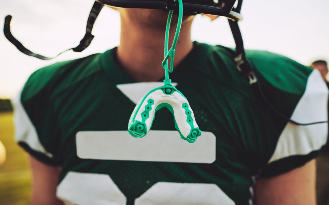 A football player carries a custom mouthguard attached to their helmet, emphasizing the role of mouthguards in preventing dental injuries during contact sports.
