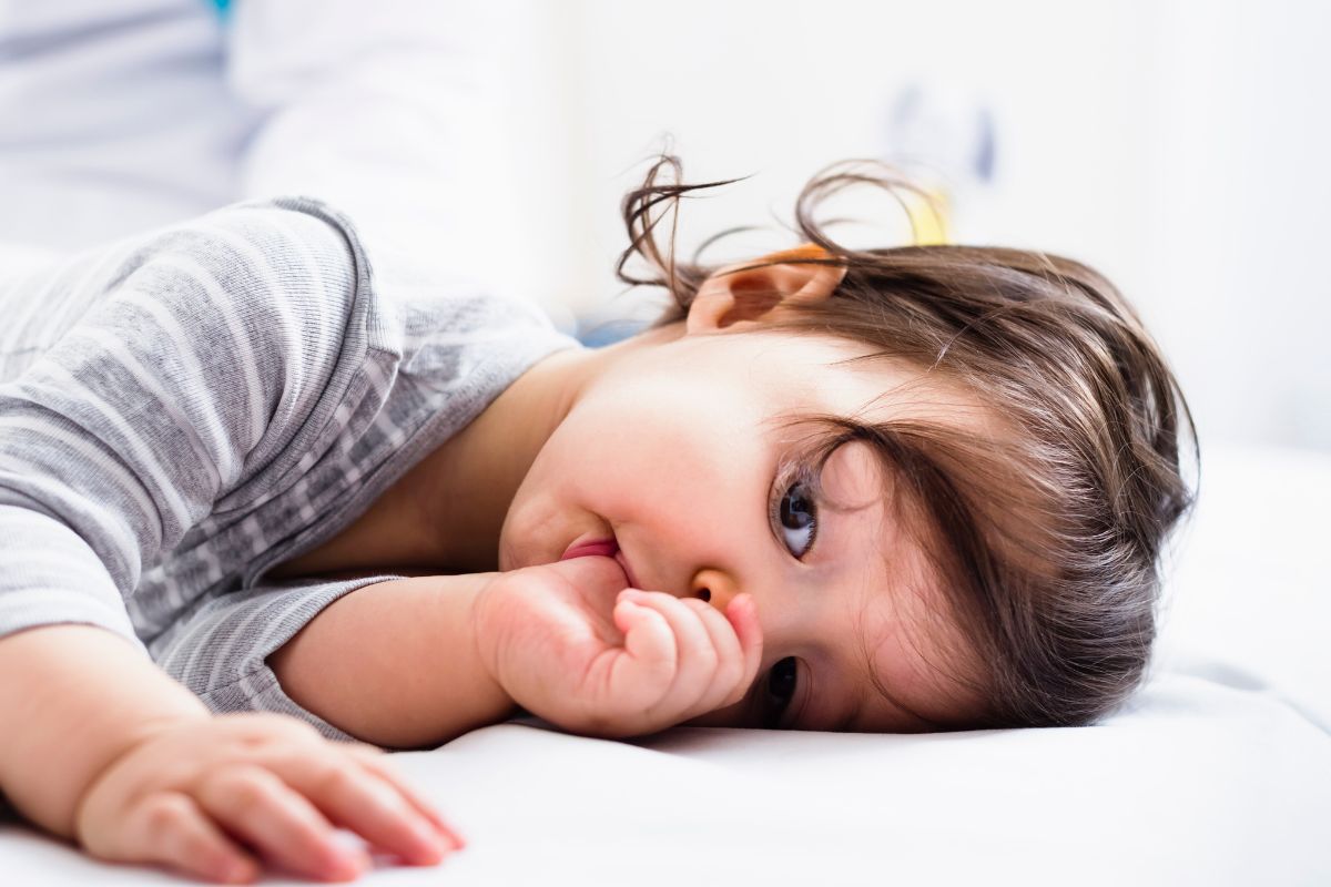 Child lying on a bed while thumb sucking, illustrating habits and sleep-disordered breathing in children that may influence facial growth and oral development.